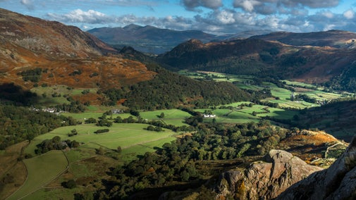 View across a valley in autumn with blue skies, green fields and autumn leaves.
